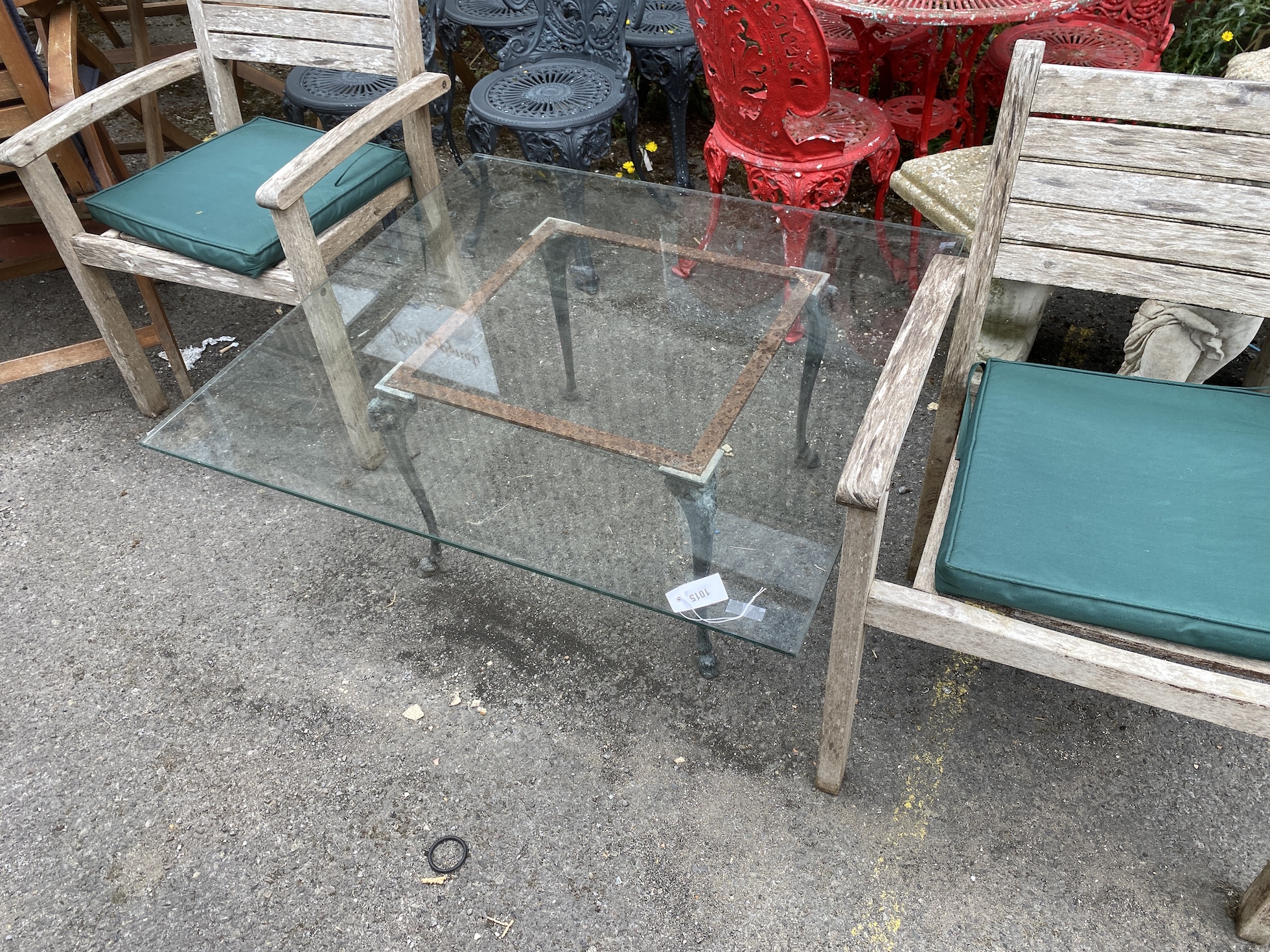 A square glass top cast metal garden table on a metal base, length 100cm, height 44cm together with a pair of teak elbow chairs